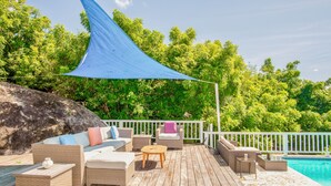 Una terraza de madera con mobiliario de mimbre, una piscina y una valla blanca.