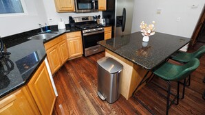 Una cucina con mobili in legno, elettrodomestici in acciaio inossidabile, un piano di lavoro in granito e un cestino.