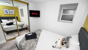 Una camera d'albergo con un letto, una TV che mostra 'NETFLIX', una finestra e uno specchio che riflette l'ambiente.