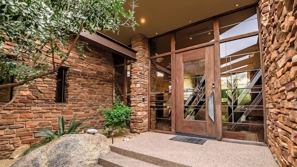 A stone building with a staircase leading to a glass door, surrounded by greenery. - Scottsdale family 4BR Oasis with Pool and Modern Living (Scottsdale)