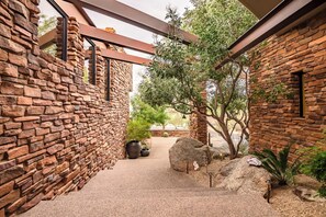Ein Korridor mit Steinwänden, einer Pergola, Topfpflanzen und einem Kaktus.
