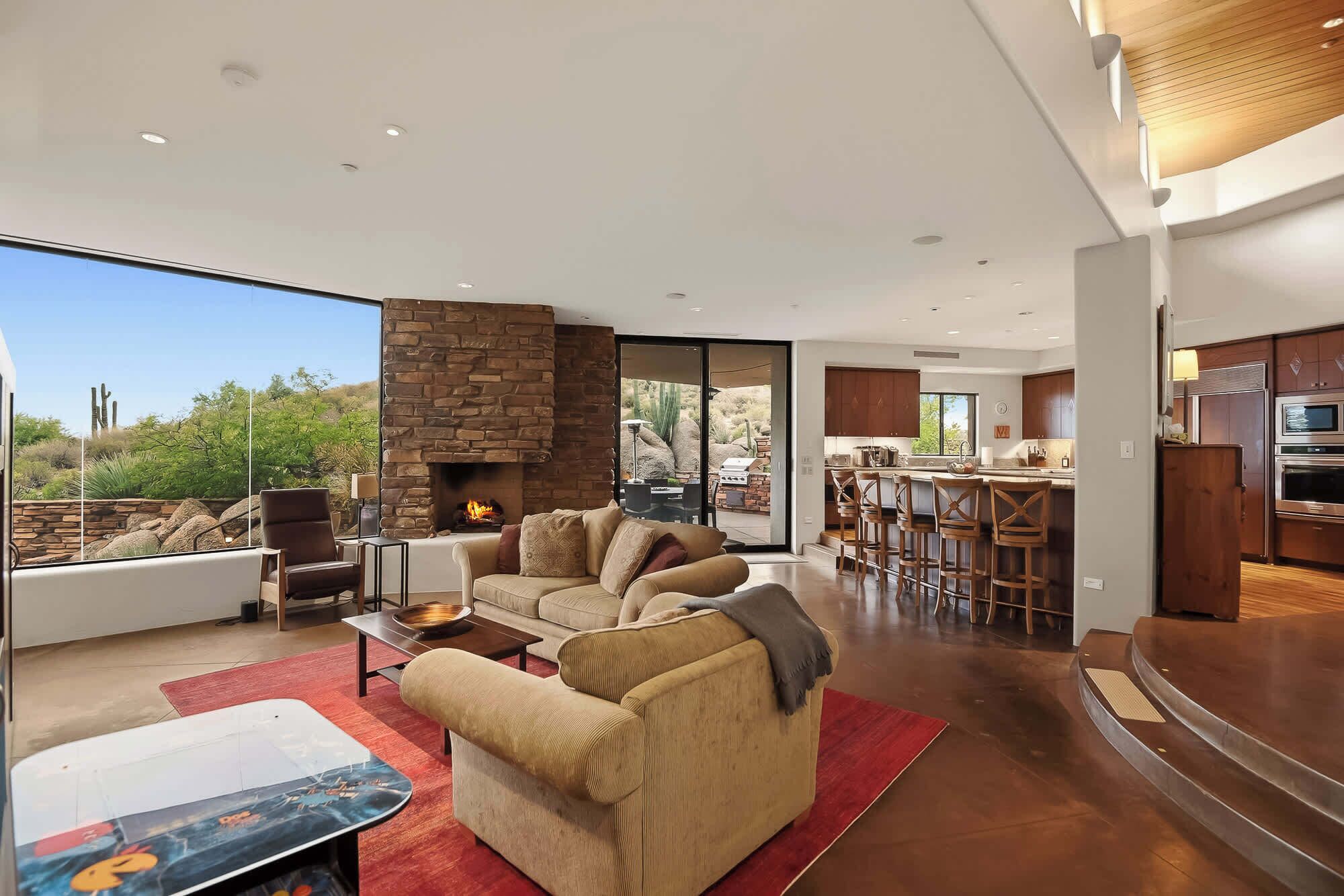 A modern living room with a stone fireplace, a dining area, and a kitchen with dark wood cabinets.