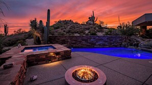A pool with a fire pit and stone walls, surrounded by desert vegetation and a sunset sky. - Scottsdale family 4BR Oasis with Pool and Modern Living (Scottsdale)