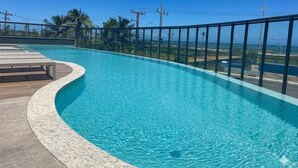 A swimming pool with a curved edge, a wooden deck, and a metal railing. - Beach Class Jaguaribe  (Salvador)