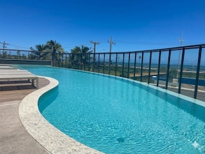 Una piscina con borde curvo, una terraza de madera y una barandilla de metal.
