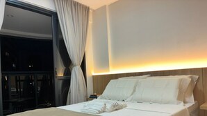 A hotel room with a bed, a nightstand, a window with curtains, and a wall-mounted light. - Beach Class Jaguaribe  (Salvador)