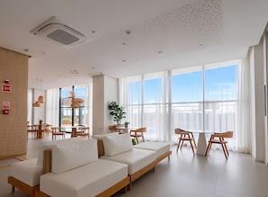 Una habitación de hotel moderna con un ventanal grande, un sofá, una zona de comedor y un techo con diseño de cuadrícula.