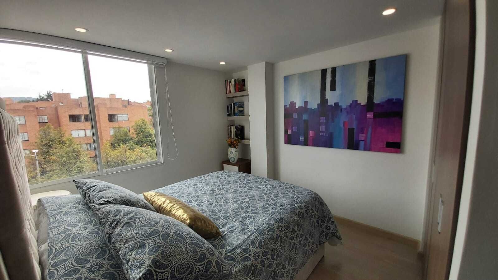A bedroom with a bed, a window, a bookshelf, and a painting.