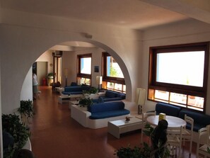 A spacious living area with blue sofas, a round table, and large windows. - Hotel Phenicusa (Lipari)