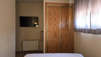 Quarto de hotel com cama, guarda-roupa de madeira, radiador e televisão na parede.