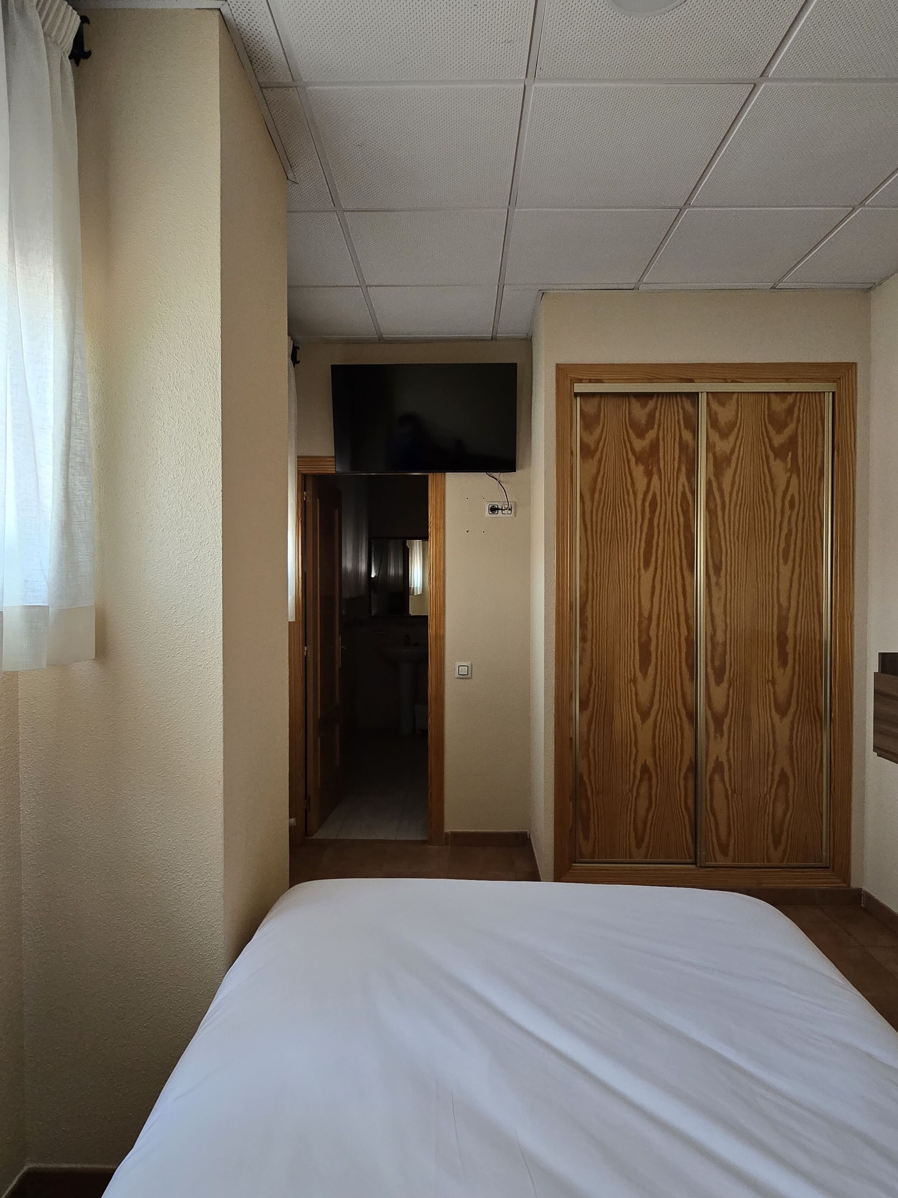 A hotel room with a bed, a television, a wardrobe, and a bathroom visible through an open door.