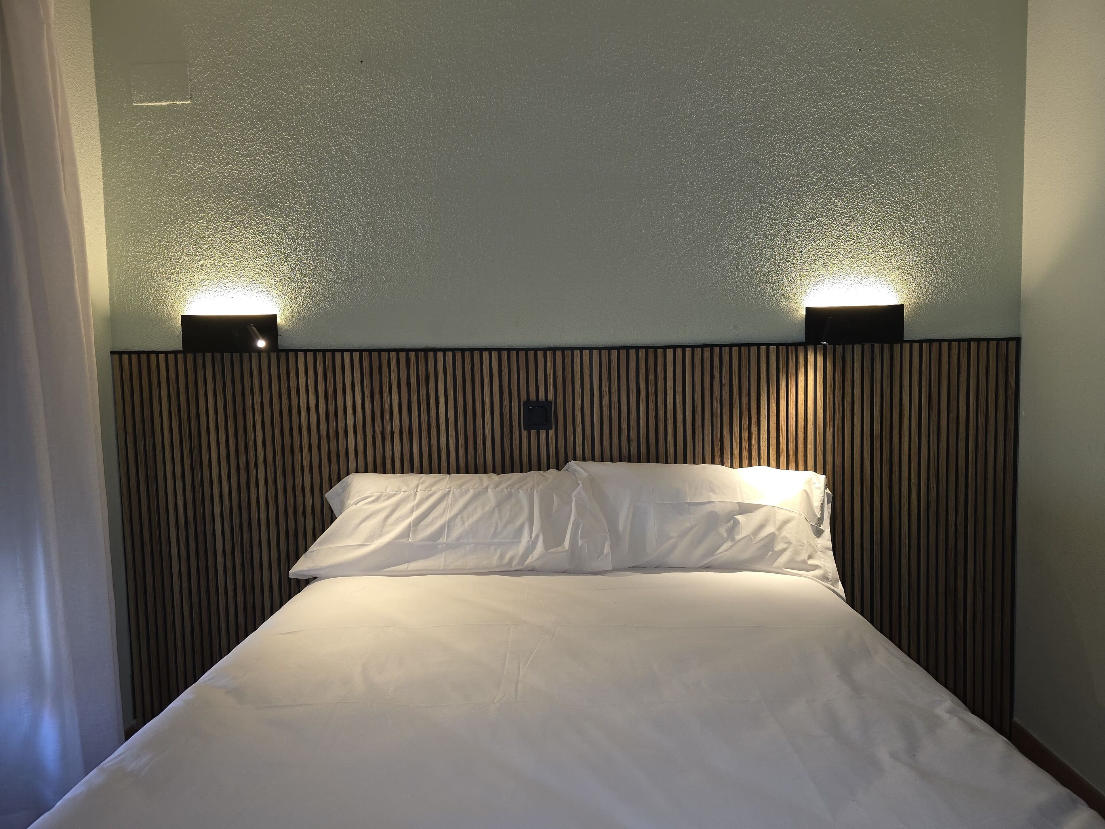 Une chambre d’hôtel avec un lit, deux lampes fixées au mur et un mur à texture.