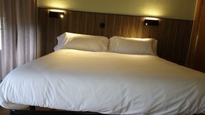 A large bed with white bedding, a wooden headboard, and two wall-mounted light fixtures. - Hostal La Cigüeña (El Espinar)