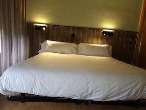 A large bed with white bedding, a wooden headboard, and two wall-mounted light fixtures.
