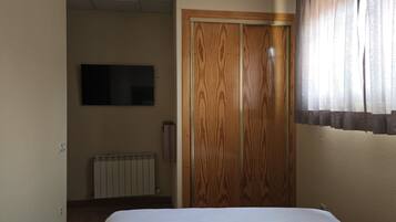 Habitación de hotel con cama, armario de madera, radiador y televisor en la pared.