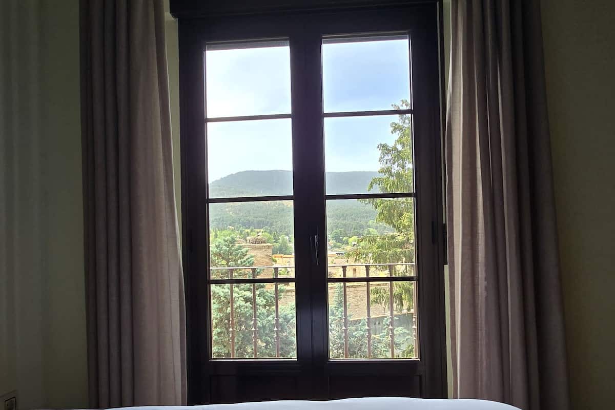 Una habitación con una cama, un ventanal con cortinas y vistas a un paisaje.