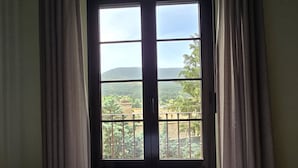 A room with a bed, a window with curtains, and a view of a landscape. - Hostal La Cigüeña (El Espinar)