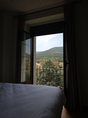 Une chambre d’hôtel avec un lit, une fenêtre avec des rideaux et une vue sur des immeubles et des collines.