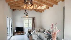 Ein geräumiges Wohnzimmer mit hoher Decke, einem großen Fenster, einer Sofagarnitur, einem Fernseher und einem Essbereich mit einem Glastisch.