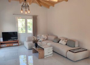 Ein Wohnzimmer mit einem Ecksofa, einem Fernseher auf einem Holzboden, einem Marmortisch und einer Kronleuchter.