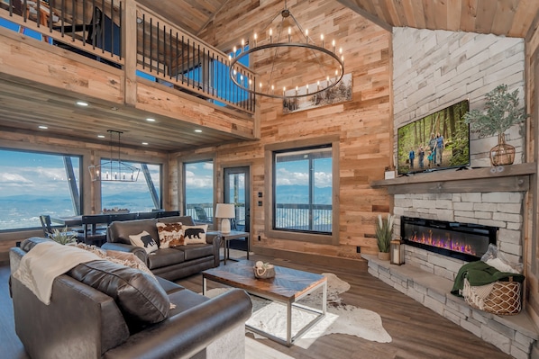Un salón espacioso con chimenea, ventanas amplias y un balcón con vistas panorámicas.
