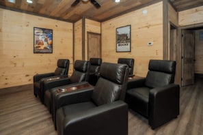 Une pièce aux murs en bois, avec un ventilateur au plafond et une porte. On y trouve quatre fauteuils en cuir noir, chacun muni d’un porte-gobelet.