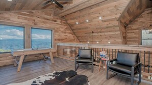 Un interno in legno con una ventola a soffitto, un'ampia finestra vista montagna, due poltrone in pelle e un tappeto in pelle di vacca.