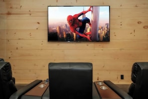 A room with a television mounted on a wooden wall, leather seating, and a cityscape view. - Indoor Pool + Panoramic Views | 4BR Sleeps 12 (Sevierville)