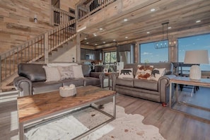 A spacious living area with a staircase, leather sofas, a coffee table, and a view of the kitchen. - Indoor Pool + Panoramic Views | 4BR Sleeps 12 (Sevierville)