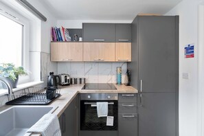 A modern kitchen with grey cabinets, a built-in oven, and a coffee machine. - Edinburgh Stay | Near City Centre | Free Parking (Edinburgh)