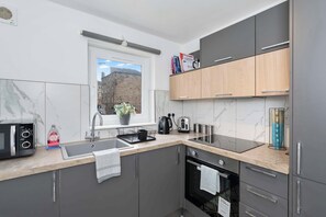 A modern kitchen with grey cabinets, a black microwave, a sink, and a window with a view of buildings. - Edinburgh Stay | Near City Centre | Free Parking (Edinburgh)