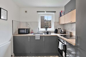 A modern kitchen with grey cabinets, a black microwave, a kettle, and a window with a view of buildings. - Edinburgh Stay | Near City Centre | Free Parking (Edinburgh)