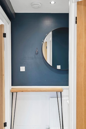 A bathroom with a dark blue wall, a round mirror, a wooden shelf, and a white radiator. - Edinburgh Stay | Near City Centre | Free Parking (Edinburgh)