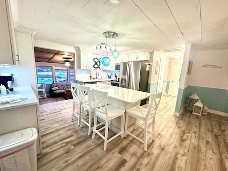 A modern kitchen with white cabinetry, a central island with chairs, and a view to the outside.