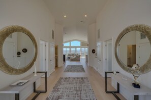 A hallway with two large mirrors, a console table, a rug, and a view to a living area.