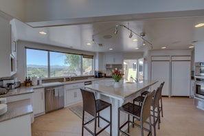 A modern kitchen with a large island, white cabinetry, and a view of the outdoors.