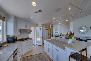 A modern kitchen with white cabinets, a central island, and a dining area with a round mirror.