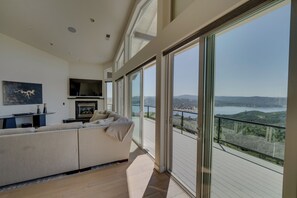 A modern living room with a sofa, a fireplace, and large windows offering a view of a lake and hills.