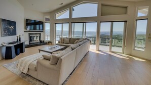 Un salon spacieux avec un grand canapé d’angle, une cheminée et un balcon offrant une vue sur les montagnes.