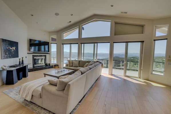 A spacious living room with a large sectional sofa, a fireplace, and a balcony with a mountain view.