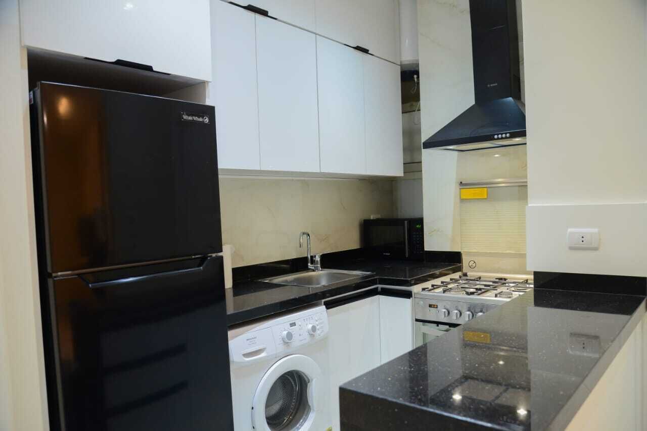 A compact kitchen with a black refrigerator, a microwave, a washing machine, and a gas stove.