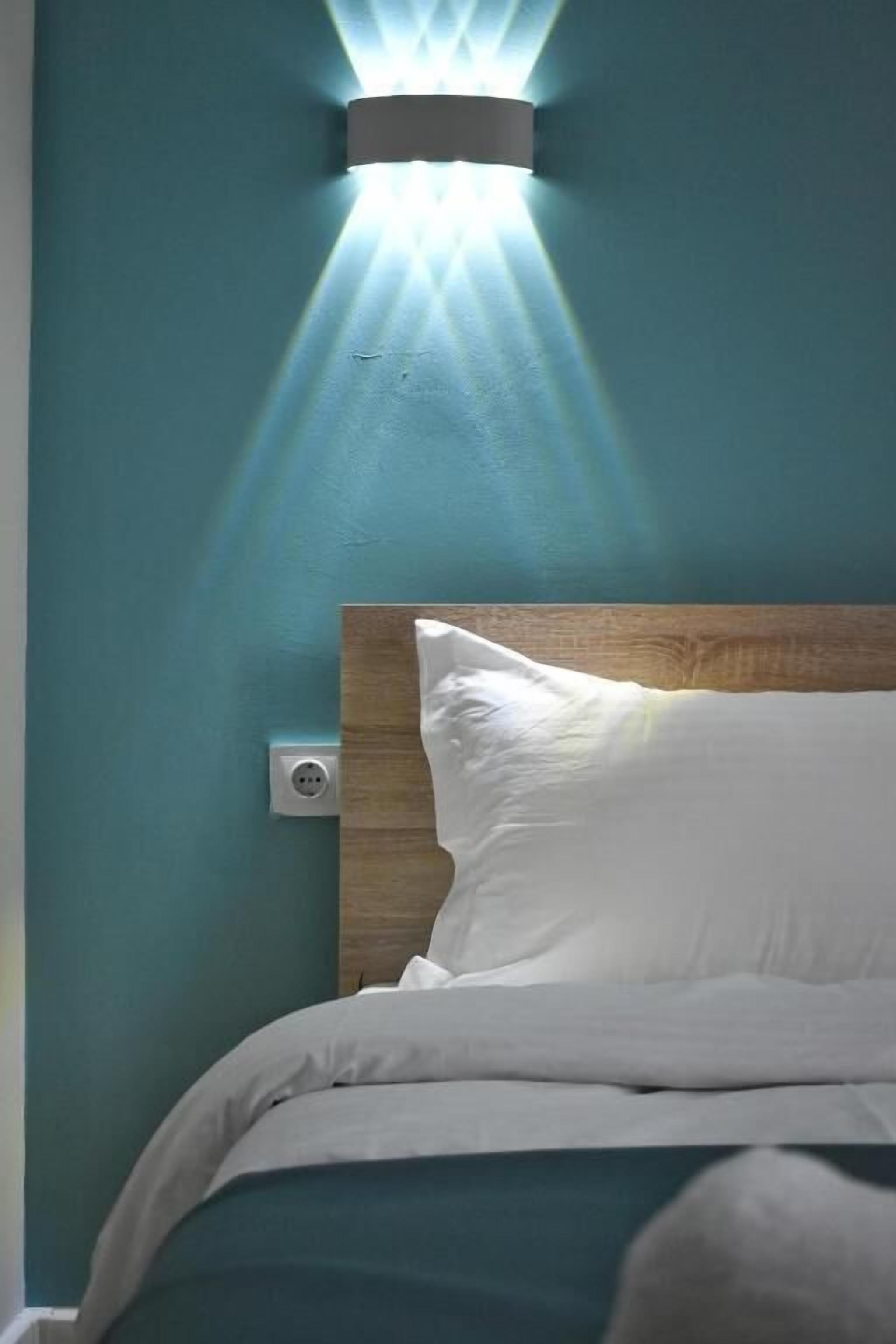 Een bed met witte beddengoed, een houten hoofdeinde en een wandlamp.