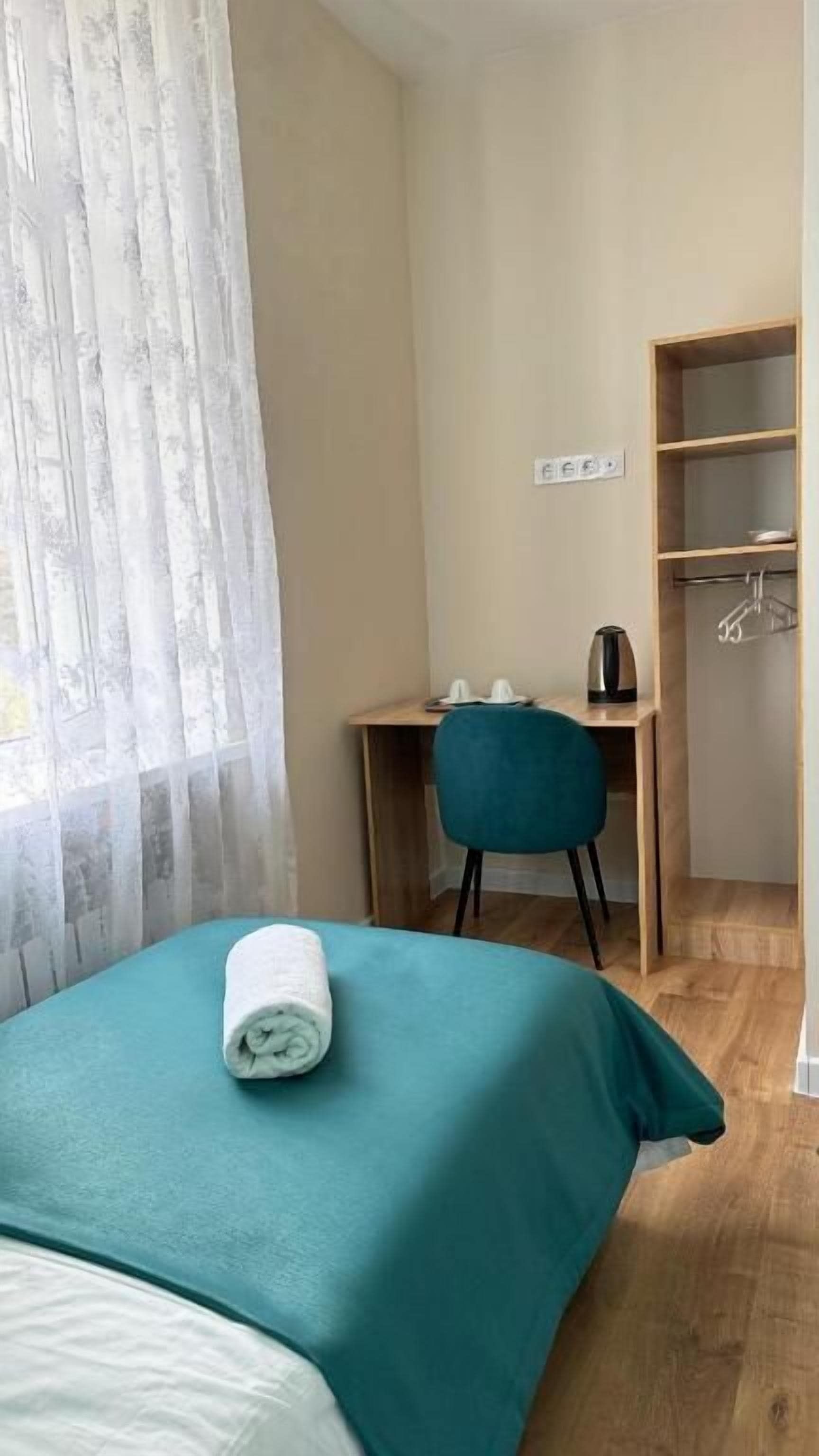 Quarto de hotel com cama, escrivaninha, cadeira, guarda-roupa e janela com cortinas.