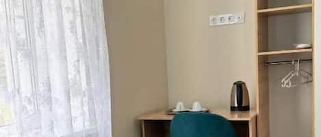 Quarto de hotel com cama, escrivaninha, cadeira, guarda-roupa e janela com cortinas.