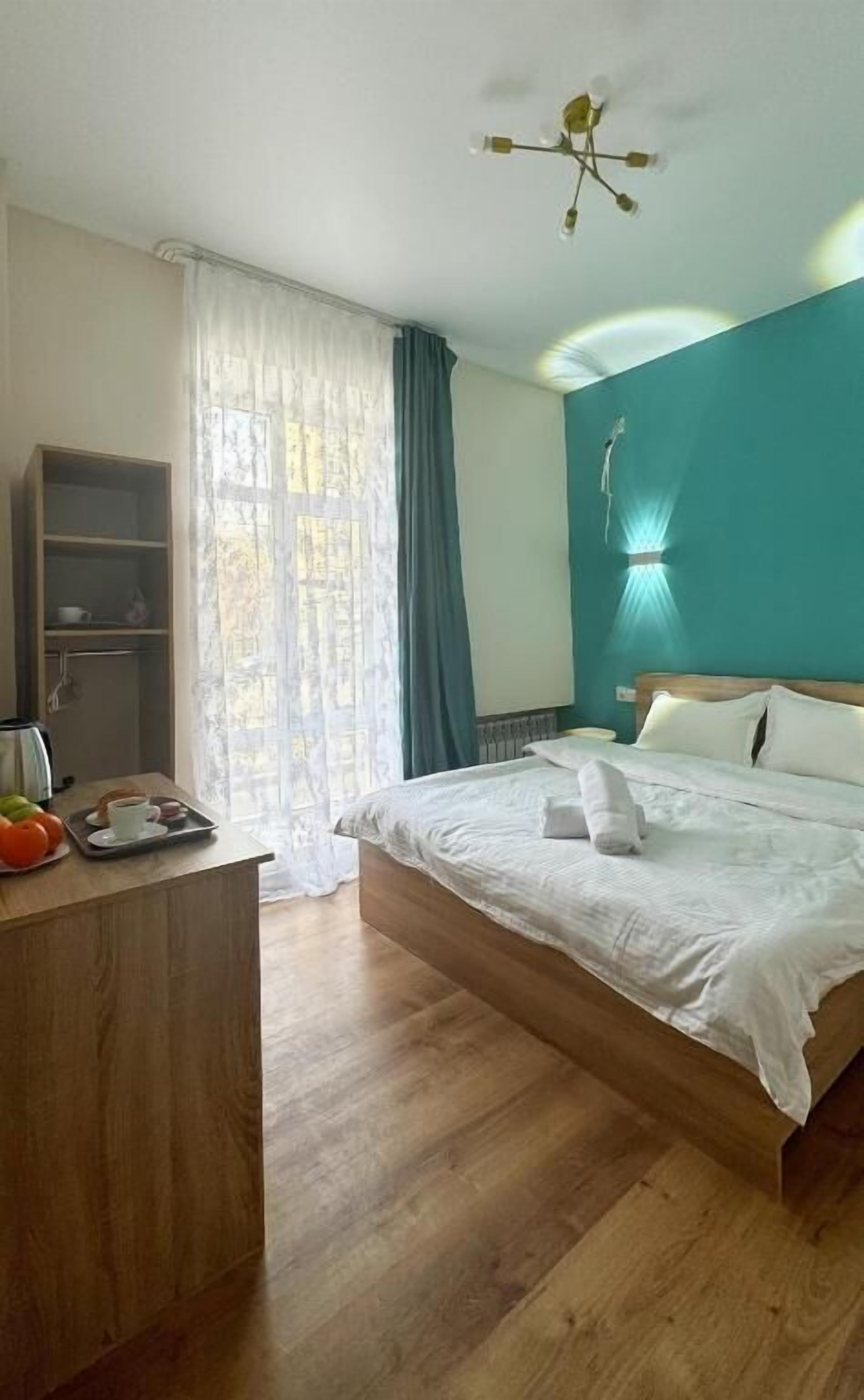 A bedroom with a bed, a desk, a shelf, and a window with curtains.