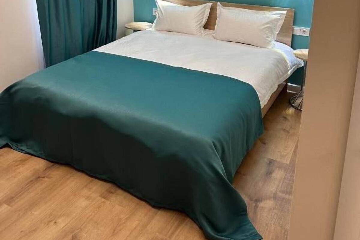 Un dormitorio con cama, paredes color turquesa y dos luces fijadas a la pared.