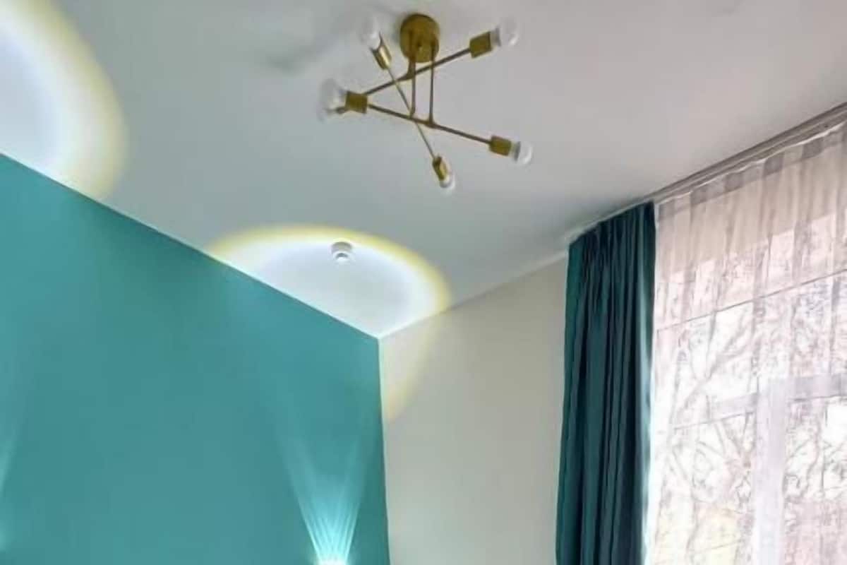 Habitación de hotel con dos camas, suelo de madera, una pared verde azulado y una ventana con cortinas.