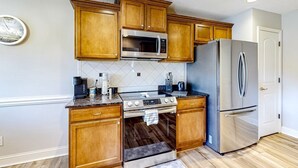 Una cocina con armarios de madera, un microondas de acero inoxidable, un refrigerador y una estufa.