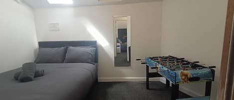 Una habitación con cama, mesa de fútbol, espejo y tragaluz.