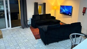 Een woonkamer met een bank, een televisie, een lamp en een schuifdeur met glas.